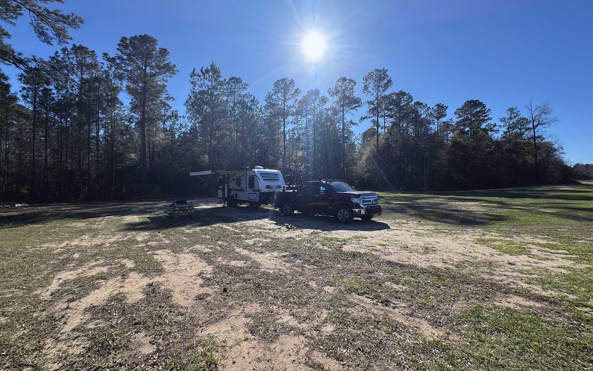 A truck and trailer in an open grassy field next to a forest